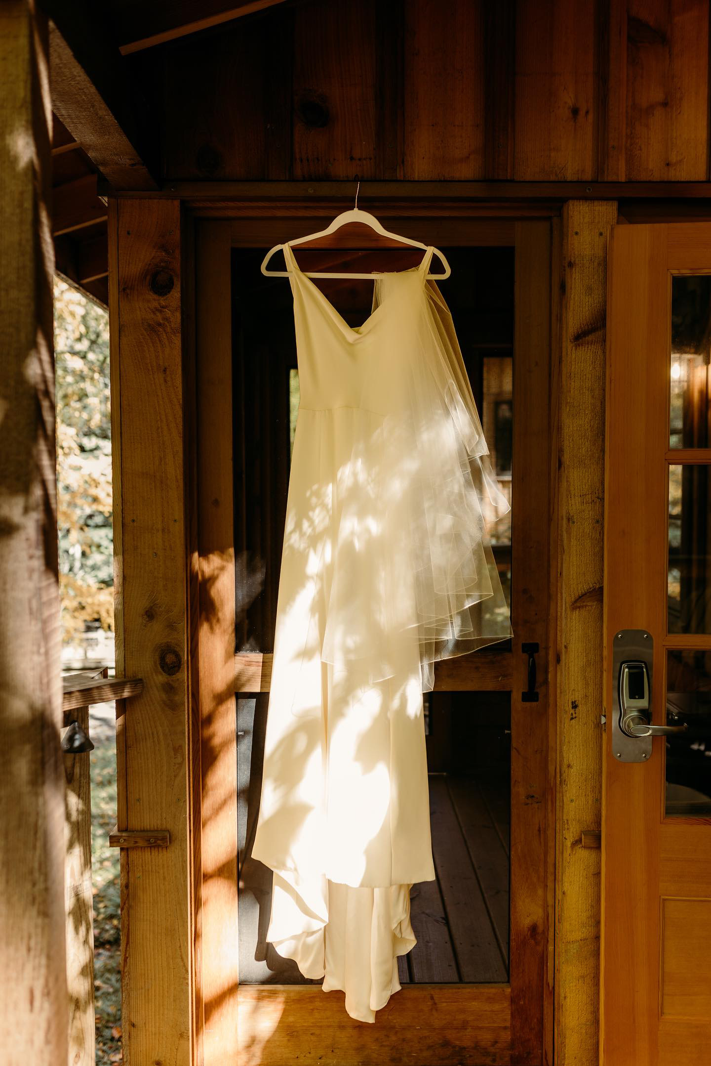 Wedding dress hanging in a sunlit treehouse doorway